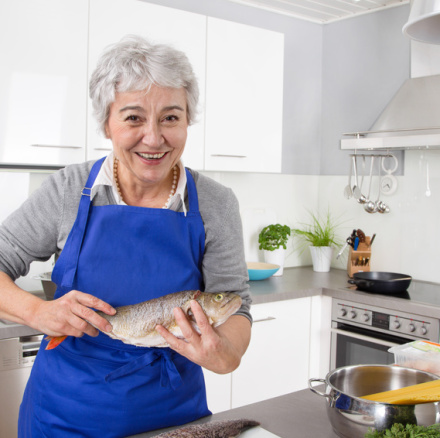 Happy senior woman in the kitchen preparing fresh fish.