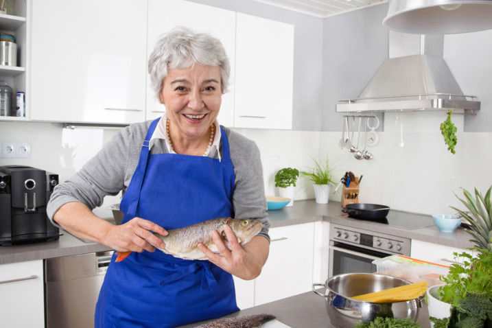 Happy senior woman in the kitchen preparing fresh fish.